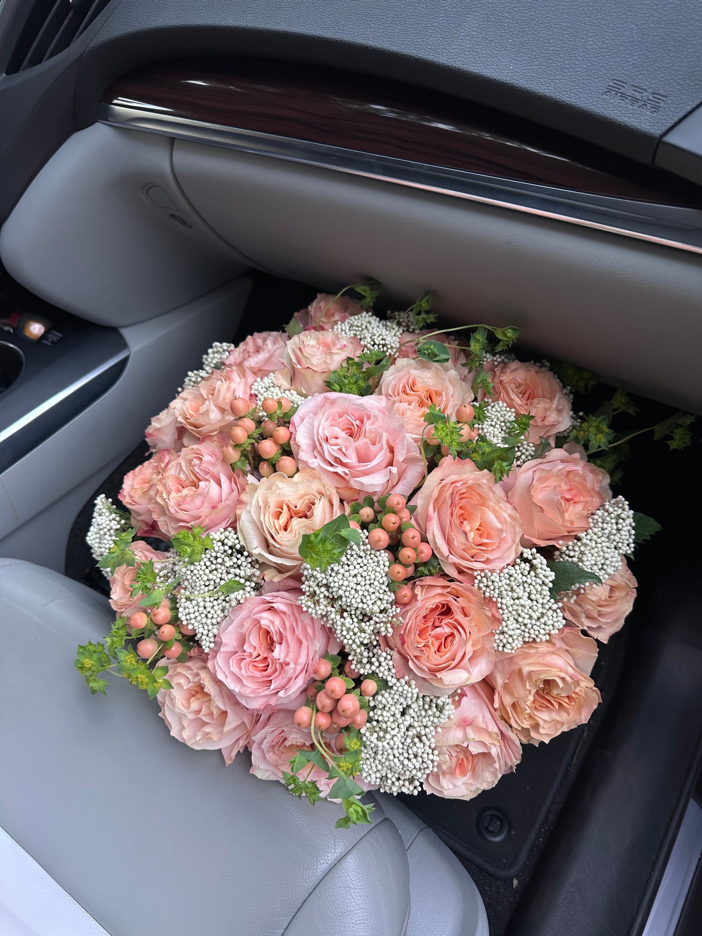 An overhead view of a round bouquet of peach and blush garden roses with berries and rice flower.