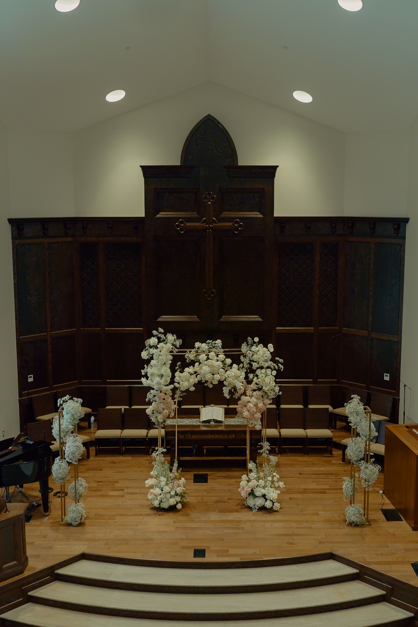 A white floral ceremony installation at a dark wood church altar